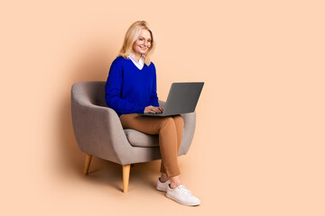 Confident mature woman working remotely in style on her laptop with a beige background, showcasing elegance and professionalism