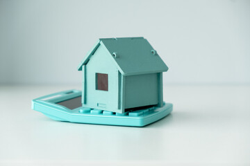 Wooden house model, calculator and coins on light table outdoors