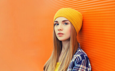 Portrait of modern young teenage blonde girl in yellow hat on orange background