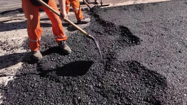 Construction workers working on a new asphalt layer on a public street.
