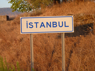 Blue 'ISTANBUL' Sign on a Metal Pole: A Bold Contrast Against the Natural Landscape of Brown Grass...