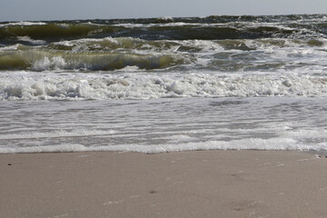 A peaceful scene of ocean waves crashing onto the sandy shoreline, with frothy white foam and dynamic green waves under a bright sky