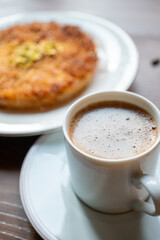 Close-up of local Turkish dessert kunefe with pistachios on a white plate and a cup of traditional Turkish coffee next to it