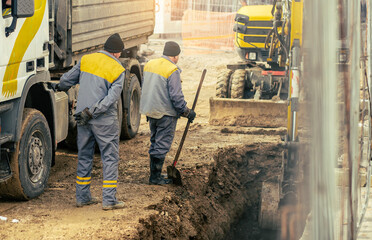 Construction workers repairing a burst water pipe under winter conditions. Excavator and truck on a...