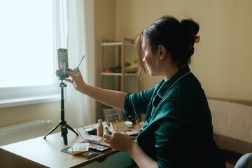 Plus size woman applying makeup on face with brush while recording vlog on smartphone for social...