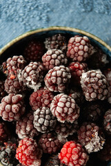 A close-up of frozen blackberries in a bowl, beautifully arranged against a dark blue background.