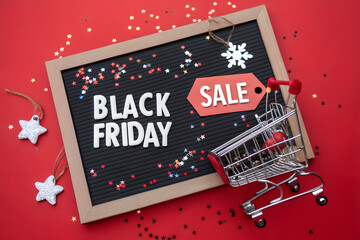 Black Friday Sale Board with Mini Shopping Cart, Star Confetti, and Festive Sale Tags on Red Background