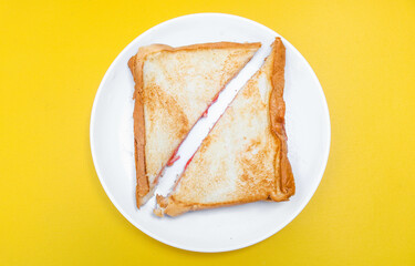 close up of white toast bread with strawberry jam on a plate, two sliced ​​bread isolated on yellow background. Simple breakfast Toast with jam