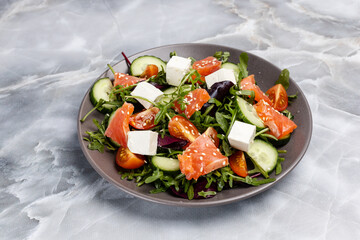 Salad with salmon, white cheese and vegetables on the plate.