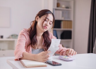 Asian woman in crisis and stress calculating expenses, costs or budget on desk at home from...
