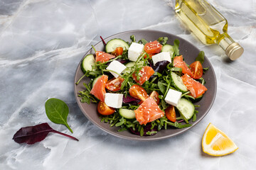 Salad with salmon, white cheese and vegetables on the plate with ingredients.