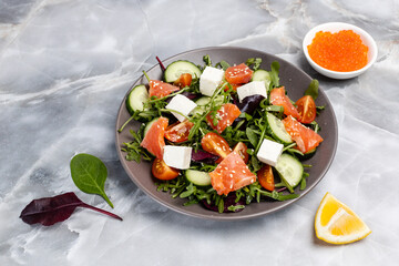 Salad with salmon, white cheese and vegetables on the plate with ingredients.