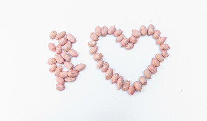 Close up Peeled peanuts isolated on white background, photo from the side. Heart shaped collection of raw nuts