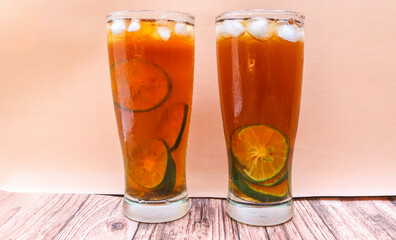 Close up Glass of iced tea with lemon, lime and ice cubes isolated on pink background and table. Two glasses of sweet iced tea filled with lemon slices