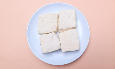 Diced fresh white tofu on a white plate isolated yellow background. Fresh soybean tofu.