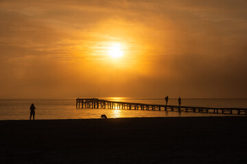 Dawn on the seashore. The beach and promenade in the morning haze are illuminated by the rising sun