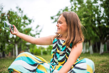 Smiling girl taking selfie with smartphone in garden