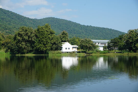 A serene lake reflects a white house and lush green hills under a clear blue sky