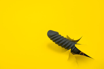 Black sex toy sticking out of yellow paper background. Copy space. 