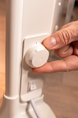 The man's hand regulates the temperature of the electric heater. Electric energy.