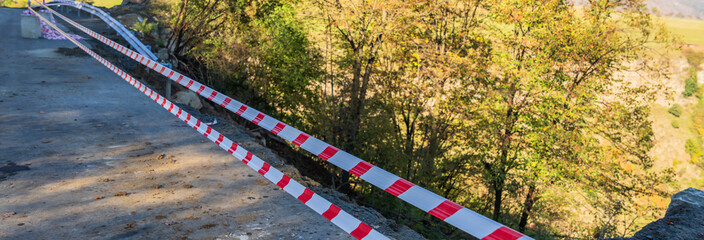 Damaged asphalt road, red tape for road construction work