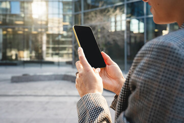 Blank screen of smart phone in hands of businesswoman on background of downtown street.