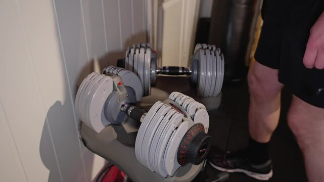 A person in home gym adjusts the weights on an adjustable dumbbell rack to prepare for a workout