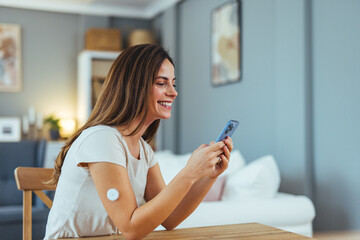 Smiling Woman Using Smartphone with Diabetes Monitor at Home