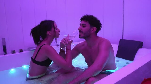 Couple toasting with champagne in a jacuzzi with purple ambient lighting.