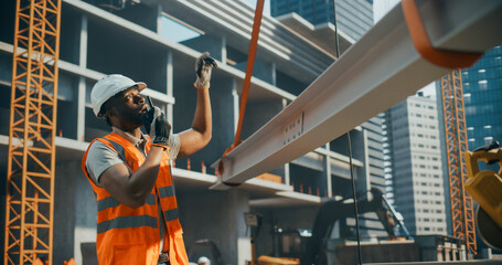 Portrait of a Handsome Black Civil Engineer Using a Radio to Communicate with a Crane Operator on a...