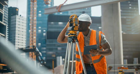 Skilled African Worker in High Visibility Vest and a Hard Hat is Designing a Building Site Layout...