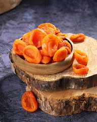 Dried apricots arranged in a rustic wooden bowl on a wooden slab in natural lighting captured indoors