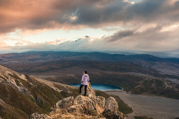 Asian hiker woman standing on Tama Lakes viewpoint with Mount Ruapehu hiding in the cloud at Tongariro national park, New Zealand