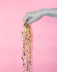 Hand holding shiny ribbon strands against a pink background in modern creative setting.