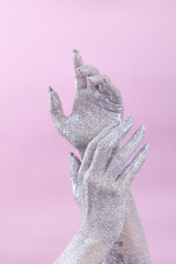 Glittering hands reaching upward against a soft pink background.