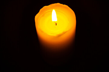 A single lit candle with a bright flame stands out against a dark, empty background. The wax is partially melted, creating a soft glow and a sense of calm and focus. The image offers strong contrast.