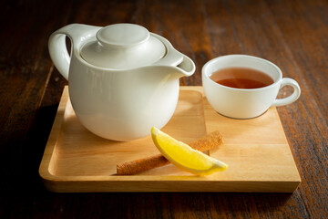 White tea set of cups and teapot featuring slice of lemon and a cinnamon stick on a wooden tray with copy space, a tea set on wooden background