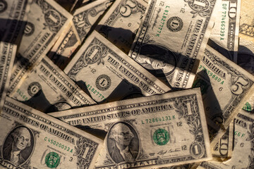 Close-up of American dollar banknotes, in one, five, ten and twenty dollar denominations, seen from above, dominated by mostly one dollar bills on top. Spread in the sun with light and shadows.