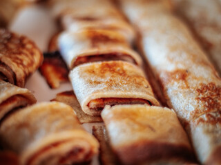 A close-up view of freshly cooked golden brown rolled pancakes, some sliced ​​to reveal the filling. The texture and crispy edges highlight their appetizing appearance.