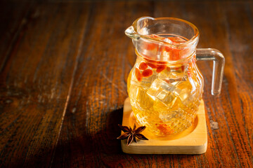 High angle shot of cold goji berries tea with ice cubes and goji berries floating in pitcher, sits on the coaster with anise pod
