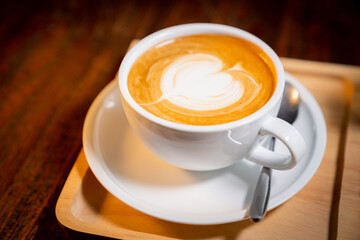 Close up shot of hot latte coffee with latte art in a ceramic white cup, saucer and spoon on wooden trays