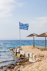 Greek Flag Waving Over Coastal Landscape With Clear Sky And Serene Waters