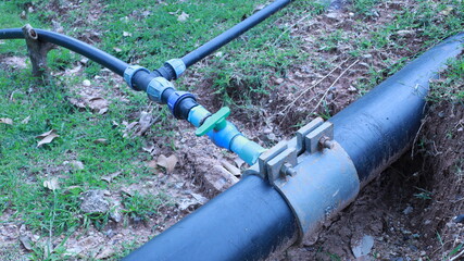 Plumbing pipe clamp. Metal clamp for reducing size of branch pipe on main water supply with valve and branch connector with ground as background with selective focus