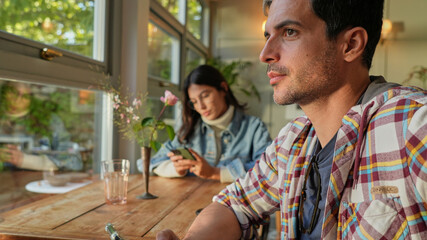 A couple relaxes in a beautifully decorated space next to the window, a woman using a phone, and a man enjoying the serene atmosphere of their home.