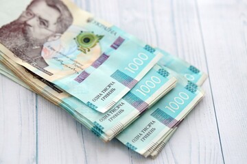 Big amount of ukrainian new one hundred hryvnia money bills with modern design on white wooden table. Financial concept, business