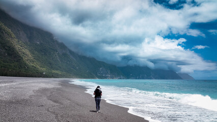 A solitary figure walking along a serene pebble beach in Taiwan under dramatic cloudy skies