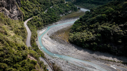 A winding road through lush mountains and a clear river in Taiwan during daylight hours