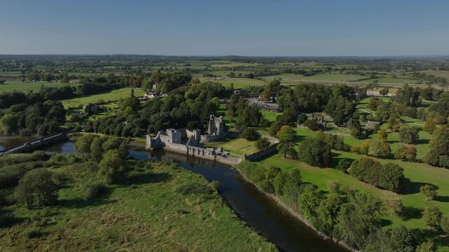 Desmond Castle, Adare, County Limerick, Ireland, September 2024. Drone orbits clockwise and pulls back to a panoramic overview of the ruined walls along the River Maigue on a clear sunny day.