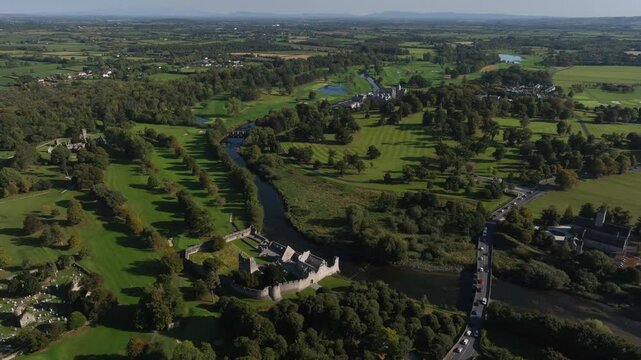 Adare, County Limerick, Ireland, September 2024. Drone orbits clockwise in an angled pullback above the scenic landscape with directional sunlight casting beautiful shadows of trees and buildings.
