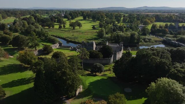 Desmond Castle, Adare, County Limerick, Ireland, September 2024. Drone orbit clockwise above manicured lawns to historic 13th century Norman ruins by the River Maigue on a bright sunny day.
